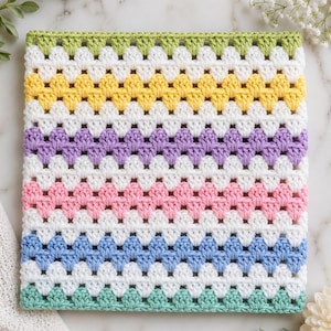 May include: A square crochet blanket featuring a repeating granny stitch pattern. The design consists of horizontal stripes in light green, yellow, lavender, pink, and blue, each separated by rows of white yarn. The texture is uniform and consistent.