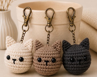 Peut inclure: Trois porte-clés en forme de tête de chat au crochet, de couleur crème, marron et noir. Chaque chat a des yeux en boutons noirs et un nez et une bouche cousus. Les porte-clés ont des fermoirs et des chaînes de couleur bronze.