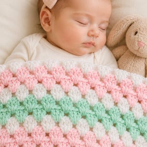 May include: A handmade crochet baby blanket featuring a repeating granny square stitch pattern in alternating horizontal stripes of soft pink, white, and mint green yarn. The blanket is textured with a classic cluster stitch design throughout.