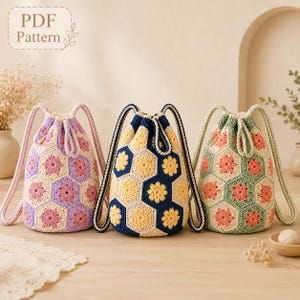 May include: Three crochet drawstring bags featuring a hexagonal floral motif. The left bag is lavender and cream with pink flowers, the center is navy and cream with yellow flowers, and the right is sage green and cream with coral flowers.