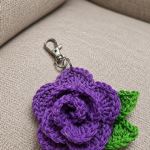 Peut inclure: Un porte-cl&eacute;s fleur crochet&eacute; violet pr&eacute;sentant un motif de rose en couches avec deux feuilles crochet&eacute;es vert vif attach&eacute;es sur le c&ocirc;t&eacute; et un fermoir mousqueton en m&eacute;tal argent&eacute; fix&eacute; au sommet de la pi&egrave;ce florale.