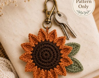 Peut inclure: Un porte-clés tournesol au crochet avec un centre marron foncé, des pétales orange et deux feuilles vertes. Le tournesol est fixé à un mousqueton en métal couleur bronze avec deux clés argentées. Une étiquette ronde porte le texte Pattern Only.