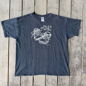 May include: A charcoal gray short-sleeve t-shirt featuring a white line-art graphic of two sneakers. The text reads, "Some of my best friends are shoes" above the illustration, with "The Bata Shoe Museum" printed in smaller text below the sneakers.