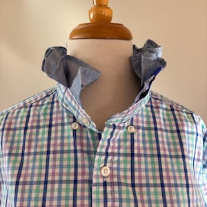 May include: A button-down shirt with a blue, green, and purple plaid pattern. The shirt has a unique ruffled collar and a small whale logo on the bottom right. The shirt is displayed on a mannequin.