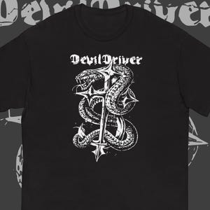 May include: A black short-sleeve t-shirt featuring a white graphic print of a snake coiled around a cross. The text "DevilDriver" is printed in a gothic-style font above the snake and cross illustration, which is centered on the chest area.