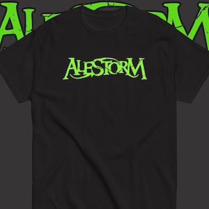 May include: A black short-sleeved t-shirt featuring the word ALESTORM printed in a distressed, bright lime green font across the chest. The same lime green text is partially visible in a larger, cropped format in the background behind the shirt.