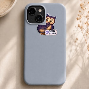 Könnte beinhalten: Eine hellgraue Smartphone-Hülle mit einem Aufkleber eines Cartoon-Eulen-Motivs mit großen Augen und braunem Gefieder. Die Eule befindet sich neben einer Sprechblase, die ein Häkchen-Symbol und den Text SEEN 2:13 AM in schwarzer Schrift enthält.