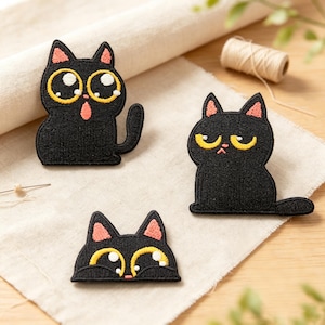 May include: Three black cat embroidered patches featuring stylized designs. One cat has wide, surprised eyes and a pink tongue, another has a grumpy expression with yellow eyes, and the third is a cat head with large, shiny eyes and pink ears.