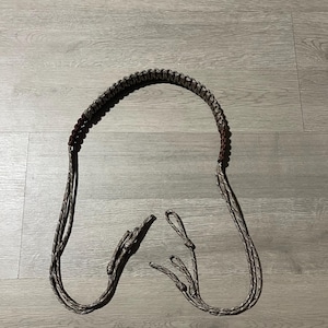 May include: A brown and gray braided paracord neck strap. The strap has a loop at each end and a braided section for the neck. The paracord is a mix of brown and gray colors.