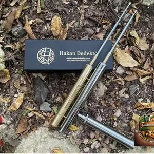 May include: Two metal detecting rods with gold and silver finishes, along with a black box with the text "Hakan Dedekt&ouml;r" and a logo. The image also includes a red seal with Turkish text and a decorative logo.