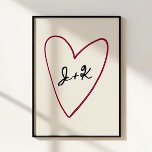Può includere: Una stampa artistica da parete incorniciata con il contorno di un cuore rosso scuro disegnato a mano su sfondo color crema. Al centro del cuore si trovano le lettere J e K scritte a mano in nero, separate da un segno più. Cornice nera sottile.