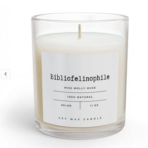 May include: A clear glass candle filled with white soy wax and a single centered wick. The white label features the text Bibliofelinophile, Miss Molly Muse, 100% Natural, 60+ HR, 11 OZ, and Soy Wax Candle in a black typewriter-style font.