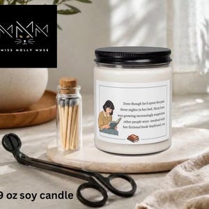 May include: A 9 oz soy candle in a clear glass jar with a black lid. The white label features an illustration of a person reading a book and text that reads: Even though he'd spent the past three nights in her bed, Mary June was growing increasingly suspicious other people were involved with her fictional book-boyfriend, too.