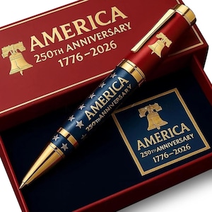 May include: A commemorative pen with a red and blue design, gold accents, and the text "AMERICA 250TH ANNIVERSARY 1776-2026." The pen is in a red box with gold lettering and a blue interior.