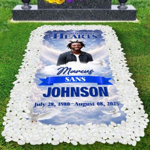 Op de afbeelding: Een gedenkplaat met een foto, engelen vleugels en duiven tegen een bewolkte hemel. De tekst luidt "Forever in our Hearts", "Marcus Sans Johnson", en de data 28 juli 1980 - 08 augustus 2025. De rand is van witte stenen.