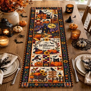 Op de afbeelding: Een rechthoekige tafelloper met Halloween-thema en een patchworkontwerp met pompoenen, zwarte katten, spoken, zonnebloemen en een spookhuis. Het middenpaneel toont de tekst The Williams Home omringd door een bloemenkrans.