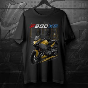 Op de afbeelding: Zwart t-shirt met een gele en grijze motorfietsafbeelding en de tekst "F900XR" in rood, wit en blauw. Het motorfietsontwerp is geplaatst tegen een stadsgezicht.