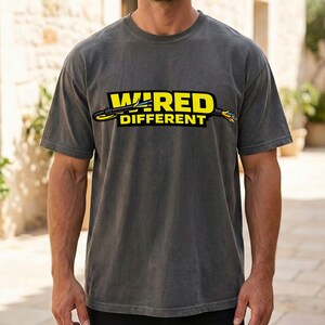 May include: A charcoal gray t-shirt with the words "WIRED DIFFERENT" in yellow and black. The graphic includes an illustration of a cable. The shirt is short-sleeved.