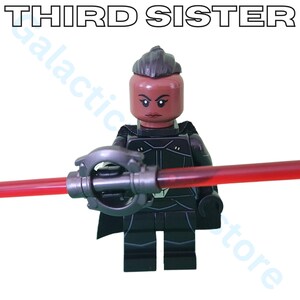 May include: A Lego figure of the Third Sister, a character from the Star Wars franchise, holding a red lightsaber. The figure is predominantly black with a dark brown head and the text "THIRD SISTER" above.