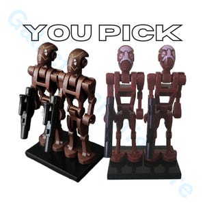 May include: Brown and red toy robot figures with black blasters, standing on black bases. The text "YOU PICK" is displayed above the figures. The figures are in a standing position.