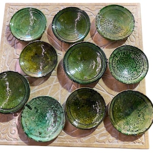 May include: A collection of nine circular ceramic bowls featuring a glossy, deep green glaze with varying textures and patterns. Each bowl has a distinct finish, ranging from smooth and reflective to crackled and mottled, arranged in a grid.