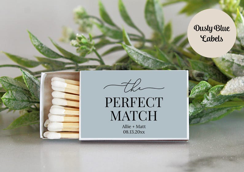 Peut inclure: Une bo&icirc;te d'allumettes rectangulaire avec une &eacute;tiquette bleu poussi&eacute;reux portant le texte "the PERFECT MATCH" en noir, ainsi que les noms "Allie + Matt" et la date "08.13.20xx". La bo&icirc;te contient des allumettes en bois &agrave; bouts blancs.