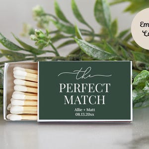 Peut inclure: Une bo&icirc;te d'allumettes rectangulaire avec une &eacute;tiquette vert fonc&eacute; portant le texte blanc "the PERFECT MATCH", les noms "Allie + Matt" et la date "08.13.20xx". La bo&icirc;te est entrouverte, r&eacute;v&eacute;lant une rang&eacute;e d'allumettes &agrave; bouts blancs.