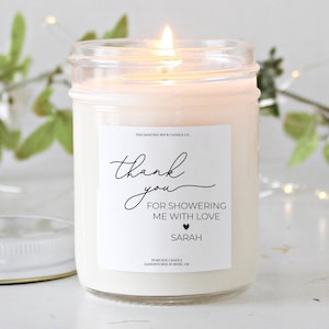 Puede incluir: Una vela de soja blanca en un tarro de vidrio transparente con una etiqueta blanca que dice "The Dancing Wick Candle Co." y "Gracias por llenarme de amor Sarah".
