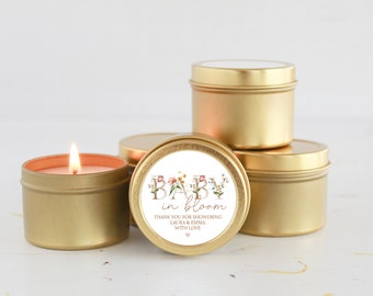 May include: Gold-colored candle tins, one lit with a flame, and others stacked. The labels read "BABY in bloom" with floral accents and a thank you message. A charming gift for a baby shower.