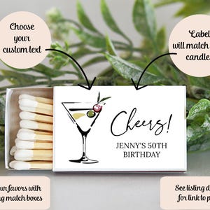 K&ouml;nnte beinhalten: Eine wei&szlig;e Streichholzschachtel mit einer Martini-Illustration und dem Text "Cheers!" und "Jenny's 50th Birthday." Die Streichholzschachtel enth&auml;lt auch den Text "W&auml;hlen Sie Ihren individuellen Text" und "Das Etikett passt zu Ihren Kerzen."