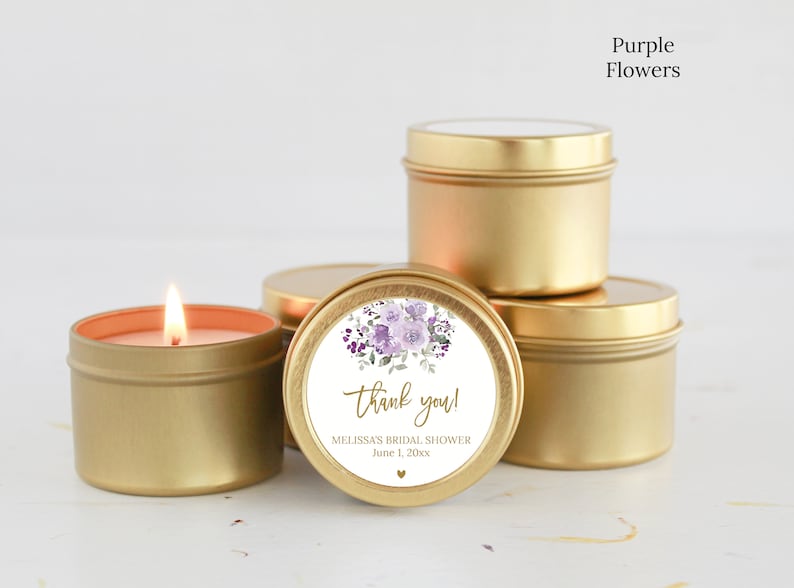 May include: A group of round gold metal candle tins, one of which is lit. A circular white label on the front features a purple floral illustration, the text "thank you!", "MELISSA'S BRIDAL SHOWER", "June 1, 20xx", and a small gold heart icon.