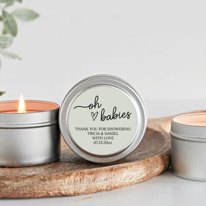 May include: Three silver candle tins with a white label. The label says "oh &hearts; babies" and "Thank you for showering Tricia & Daniel with love 07.25.20xx".