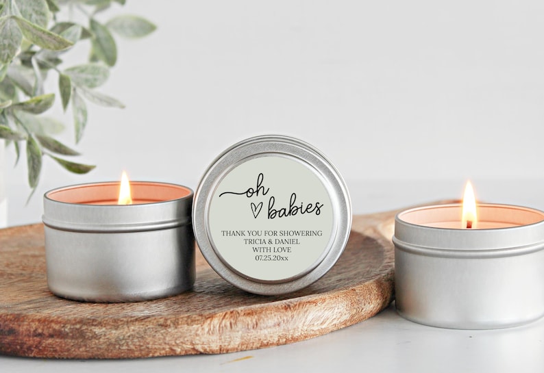 May include: Three silver candle tins with a white label. The label says "oh &hearts; babies" and "Thank you for showering Tricia & Daniel with love 07.25.20xx".