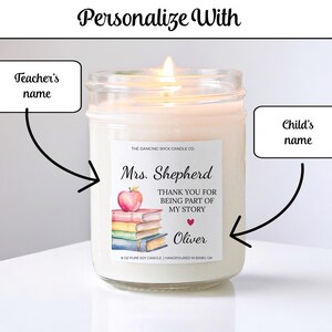 May include: A lit, white soy candle in a glass jar. The label reads "Mrs. Shepherd, THANK YOU FOR BEING PART OF MY STORY, Oliver" with an apple and books graphic. The candle is hand-poured in Bixby, OK. The text "Personalize With" is at the top.