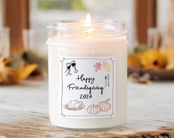 May include: A white candle in a clear glass jar with a label that says "Happy Friendsgiving 2024". The label has illustrations of wine glasses, a turkey, pumpkins, and fall leaves.