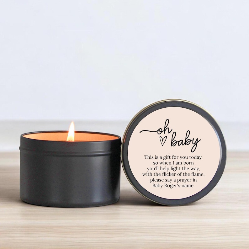 May include: A black candle in a tin with a pink label that says "oh baby" with a heart and the text "This is a gift for you today, so when I am born you'll help light the way, with the flicker of the flame, please say a prayer in Baby Roger's name."