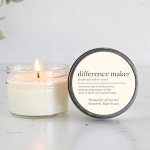 May include: A white candle in a clear glass jar with a silver lid. The lid has a black and white label that reads "difference maker (di-farn(t)s mak-er; noun) someone that is dedicated to making a big impact in the lives of those who need it most Thanks for all you do! Sincerely, Mike Evans"