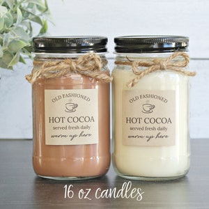 May include: Two 16 ounce glass candle jars with black lids and twine bows. The labels are brown with white text that reads "Old Fashioned Hot Cocoa served fresh daily warm up here".