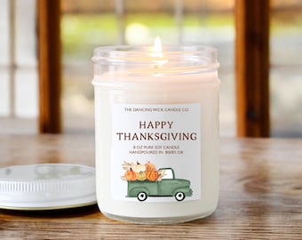 May include: A clear glass jar candle with a white label that reads "THE DANCING WICK CANDLE CO. HAPPY THANKSGIVING 8 OZ PURE SOY CANDLE HANDPOURED IN BIXBY, OK". The label also features a watercolor illustration of a green pickup truck carrying pumpkins.