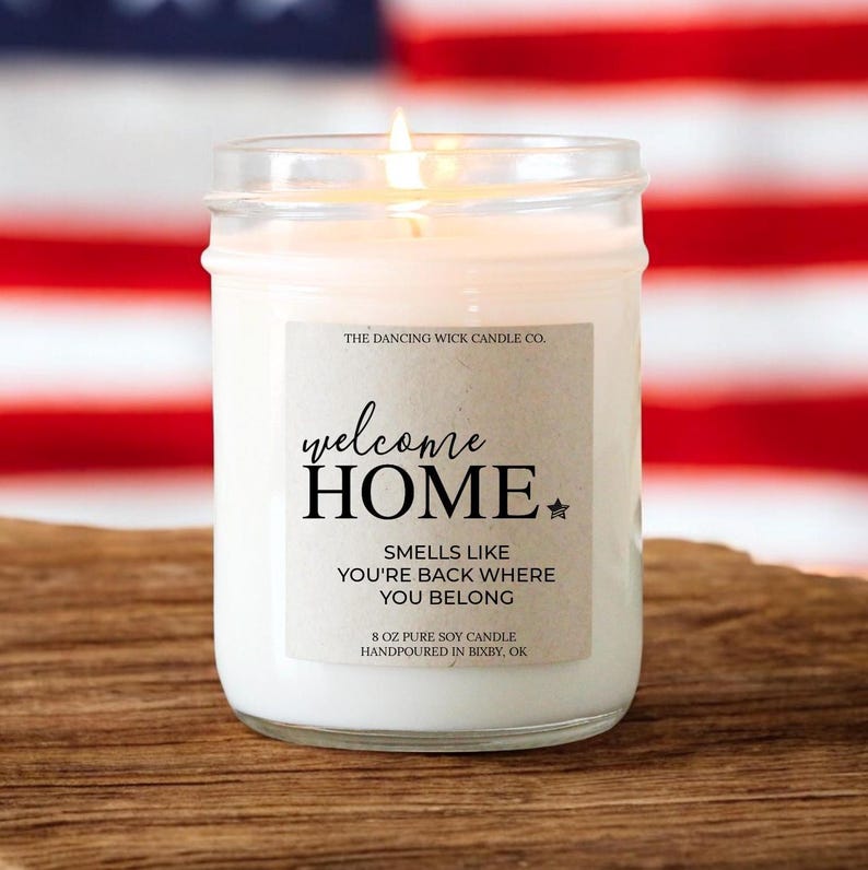 May include: A glass jar candle with a brown label that reads "welcome HOME" with a star. The label also says "Smells like you're back where you belong" and "8 oz pure soy candle handpoured in Bixby, OK".
