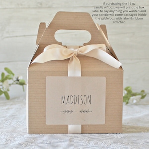 May include: A small, light brown gable box with a handle, tied with a cream-colored ribbon. A rectangular label on the front reads "MADDISON" in black, with leaf accents. The text on the box says, "If purchasing the 16 oz candle w/ box..."