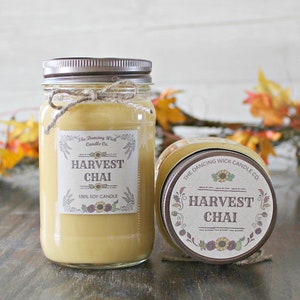 K&ouml;nnte beinhalten: Zwei Glasbeh&auml;lter mit braunen Deckeln und Etiketten. Die Etiketten zeigen "The Dancing Wick Candle Co." und "Harvest Chai 100% Soy Candle".