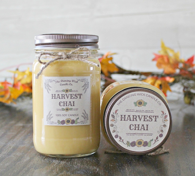 K&ouml;nnte beinhalten: Zwei Glasbeh&auml;lter mit braunen Deckeln und Etiketten. Die Etiketten zeigen "The Dancing Wick Candle Co." und "Harvest Chai 100% Soy Candle".