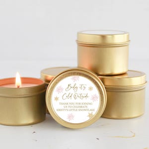 May include: Gold candle tins with a white label that says "Baby it's Cold Outside" and "Thank you for joining us to celebrate Kristy's Little Snowflake".