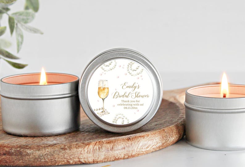 May include: Three silver candle tins with white labels. The center label has gold text that reads "Emily's Bridal Shower" and "Thank you for celebrating with us! 08.13.2023". The label also features a watercolor illustration of a champagne flute with a pearl necklace.