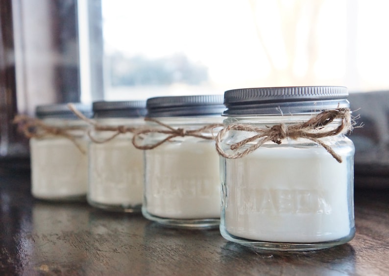 May include: Four glass jars with silver lids and white candles inside. Each jar is tied with a brown twine bow.