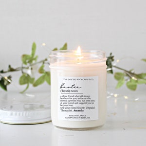 May include: A clear glass jar candle with a white label that reads "THE DANCING WICK CANDLE CO. bestie ('besti) noun a close friend who will always be there for you; a ride-or-die friend; a person who has seen you at your worst and support you to be your best. see also: Soul Sister; Unpaid Therapist. Amanda PURE SOY CANDLE HANDPOURED IN BIXBY, OK"