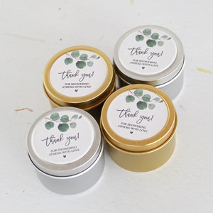 May include: Four round metal tins in gold and silver finishes, each topped with a circular white label featuring a watercolor eucalyptus branch illustration and the text: thank you! FOR SHOWERING ATHENA WITH LOVE, finished with a small heart icon.