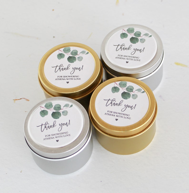 May include: Four round metal tins in gold and silver finishes, each topped with a circular white label featuring a watercolor eucalyptus branch illustration and the text: thank you! FOR SHOWERING ATHENA WITH LOVE, finished with a small heart icon.