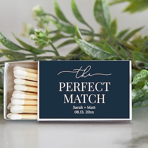 May include: A navy blue matchbox with white text that reads "the perfect match" with the names Sarah + Matt and the date 08.13.20xx.